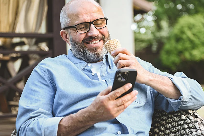 Szczęśliwy i zrelaksowany mężczyzna na fotelu przegląda telefon.