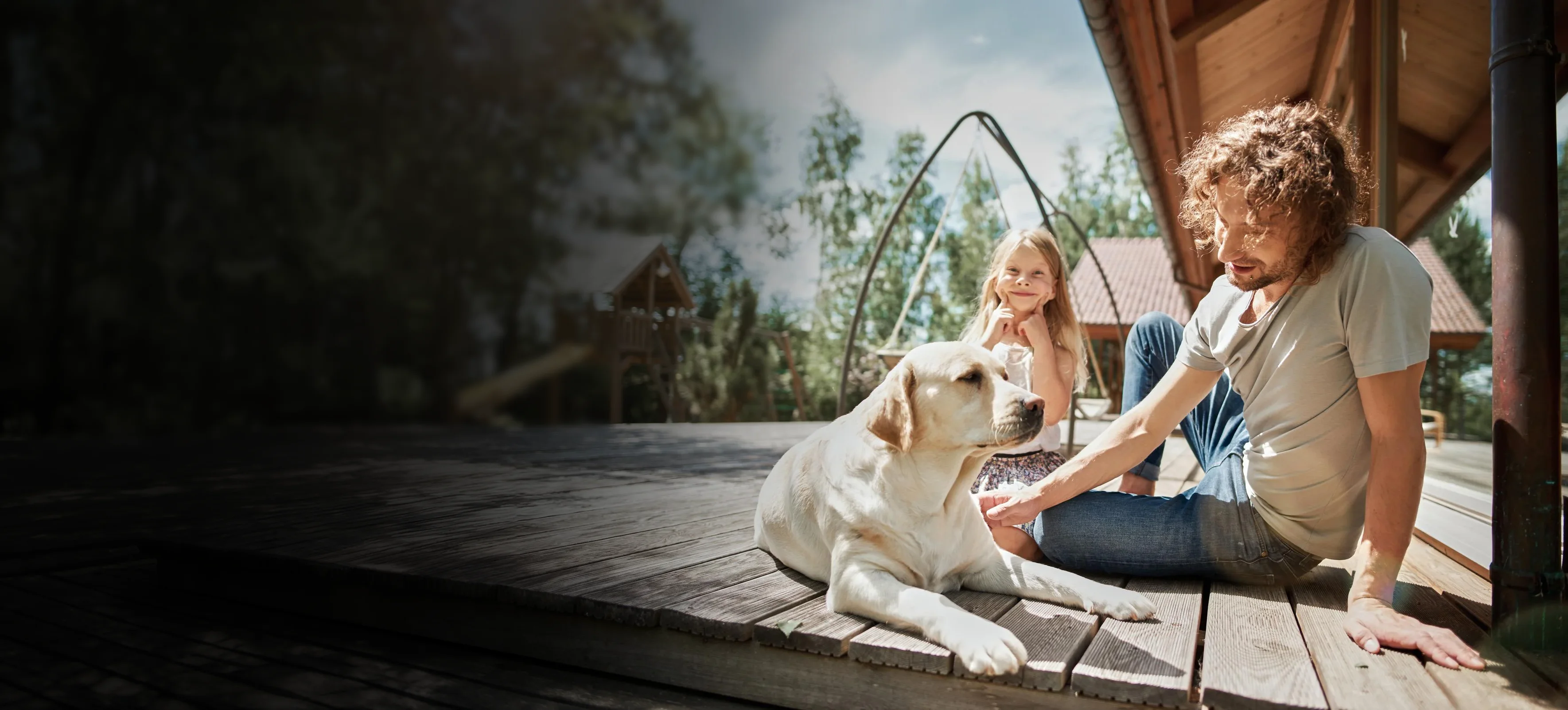 Uśmiechnięta dziewczynka oraz jej tata bawią się ze swoim psem na tarasie.