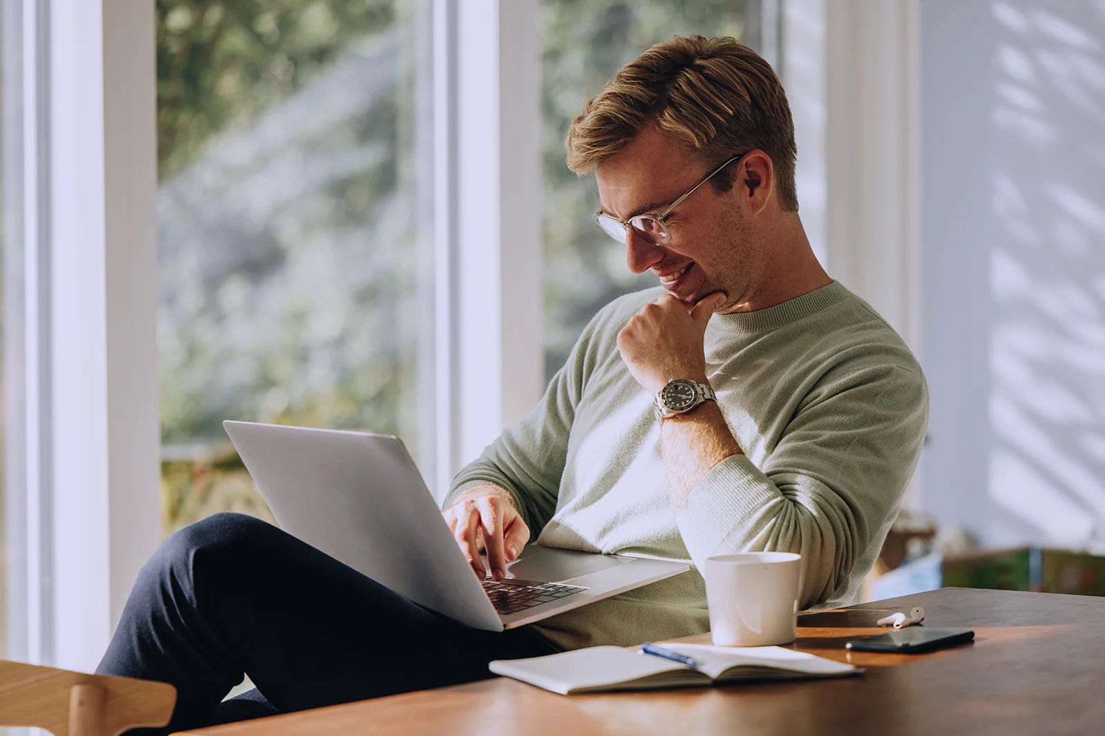 Uśmiechnięty mężczyzna przegląda swój komputer, popijając kawę.