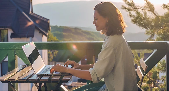 Skupiona kobieta pracuje przy komputerze na balkonie przy zachodzie słońca.
