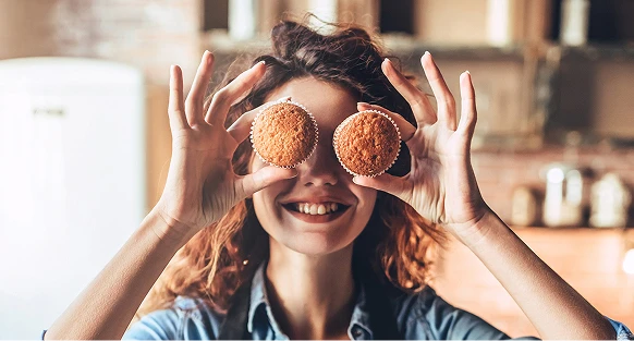Uśmiechnięta dziewczyna pokazuje dwie wypieczone babeczki, ustawia je na wysokości oczu jakoby miałyby imitować okulary.
