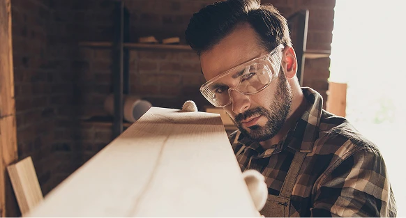 Mężczyzna w skupieniu obserwuje spolerowany wcześniej kawałek drewna.