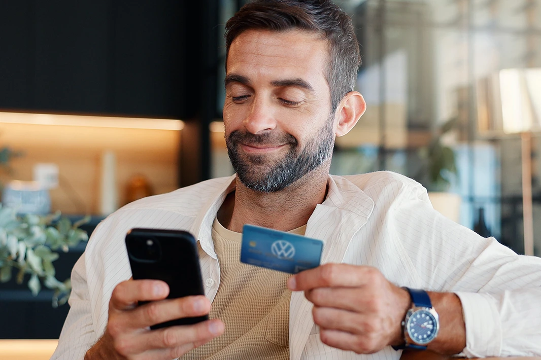 Zadowolony z życia mężczyzna płaci za zakupy w Internecie swoją kartą do konta.